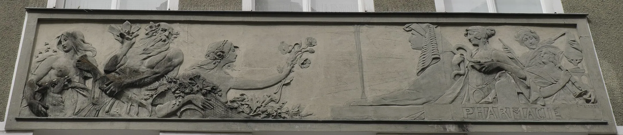 Steinrelief an der Fassade der Stadt-Apotheke: allegorische Figuren mit Blüten und Heilpflanzen, rechts Figuren mit Äskulapstab und die Inschrift „Pharmacie“