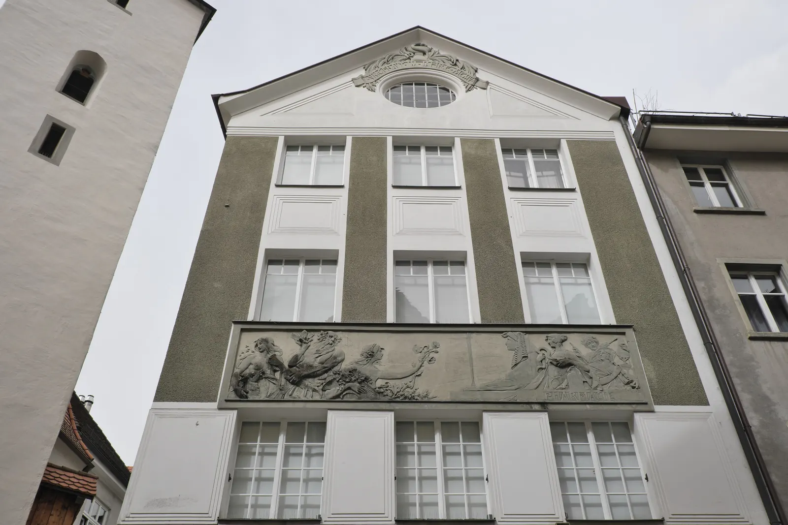 Obergeschosse der Stadt-Apotheke mit salbeigrünen Wandfeldern, weißen Fensterachsen, Relief-Fries und Giebel mit Rundfenster und Stuckkartusche