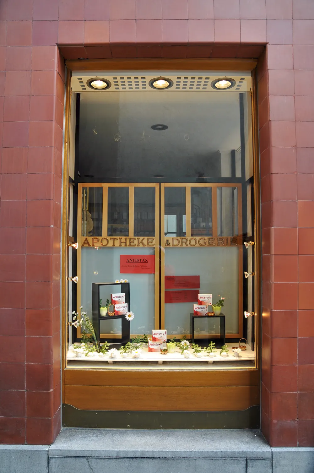 Schaufenster der Stadt-Apotheke in der roten Fliesenfassade mit Holzrahmen und der Aufschrift „Apotheke · Drogerie“